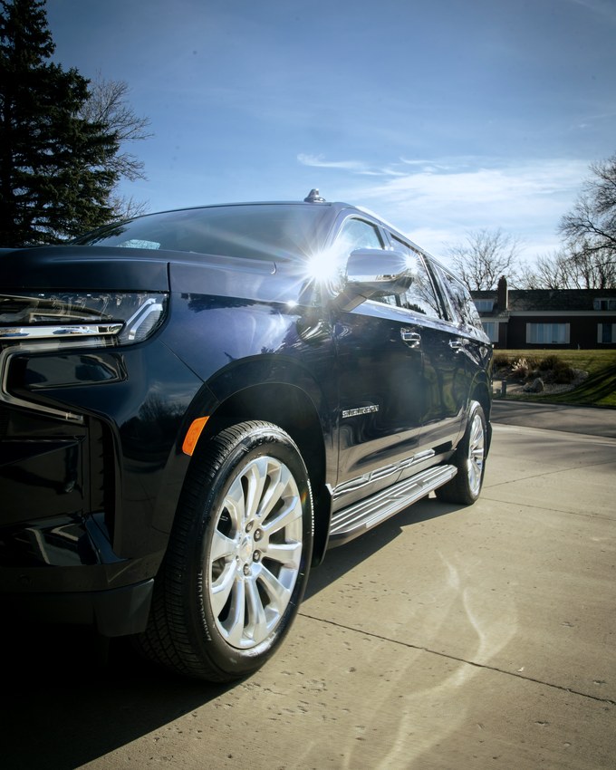 A dark Chevrolet Suburban front three quarter in low sun, whole car in frame.