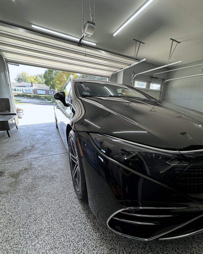 A black Mercedes EQS in the studio, overhead light drawing a clean line down the hood.