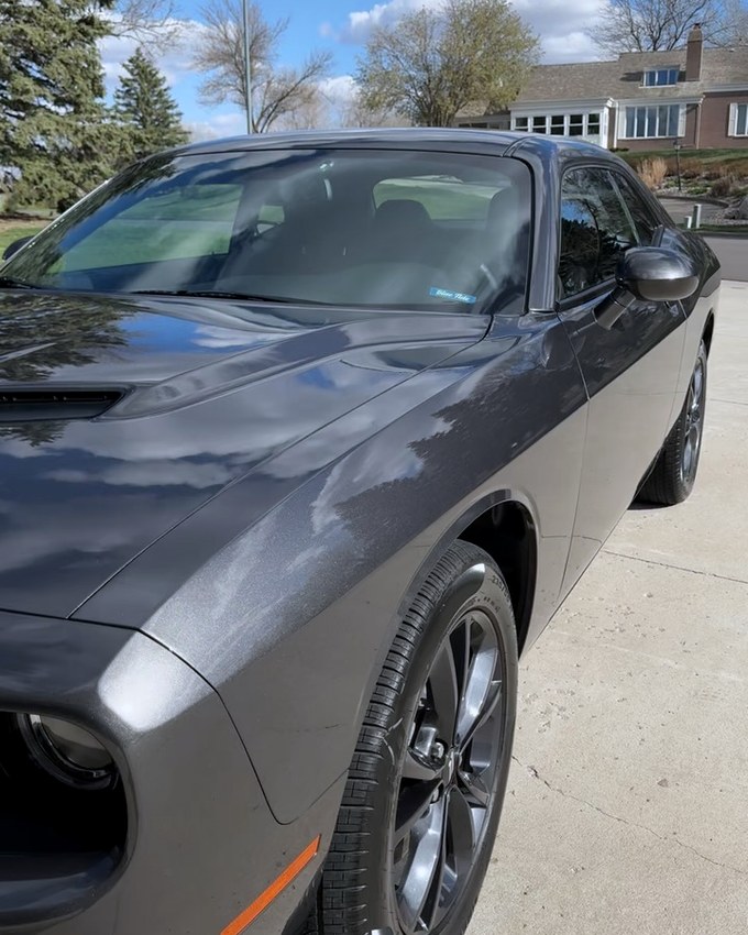 A grey Dodge Challenger front three quarter with cloud reflected across the bonnet.