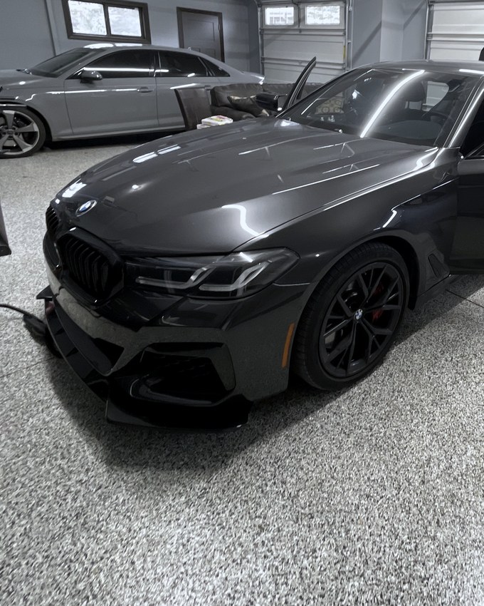 A dark grey BMW 5 Series in the studio, hood and wing holding a clean reflection.