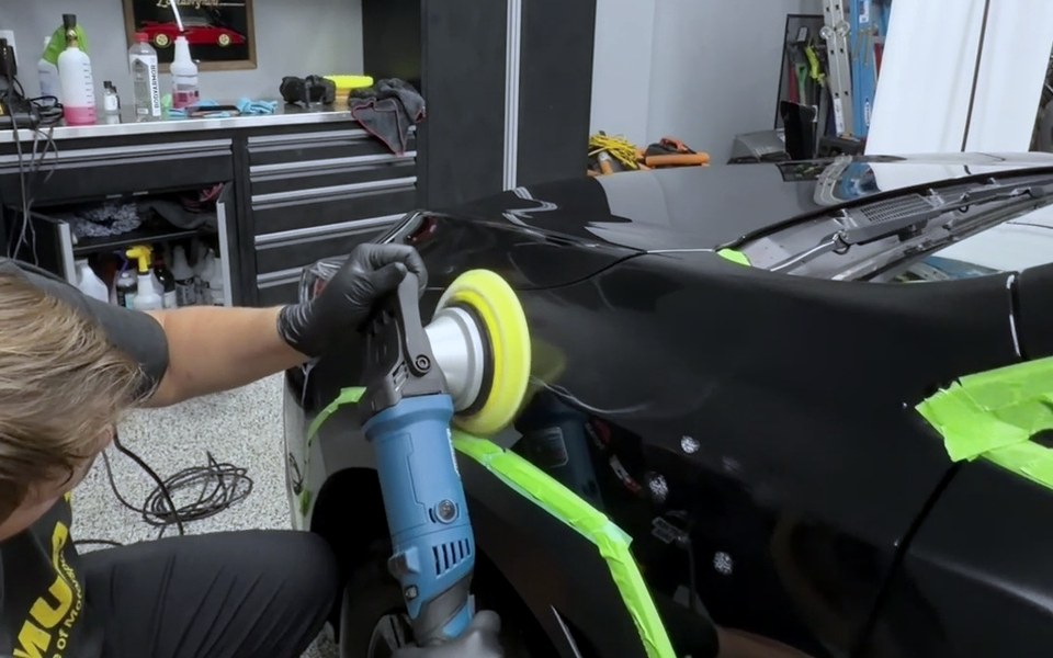 A Master Shine technician in branded uniform and nitrile gloves runs a dual action polisher across a masked panel in the studio.