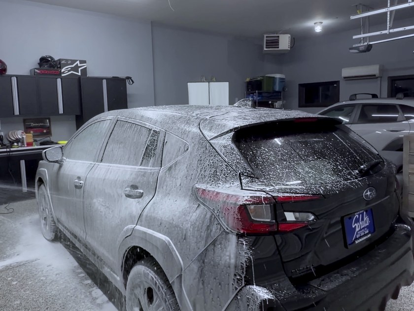 A vehicle covered in wash foam inside the studio bay, the floor wet and clean.